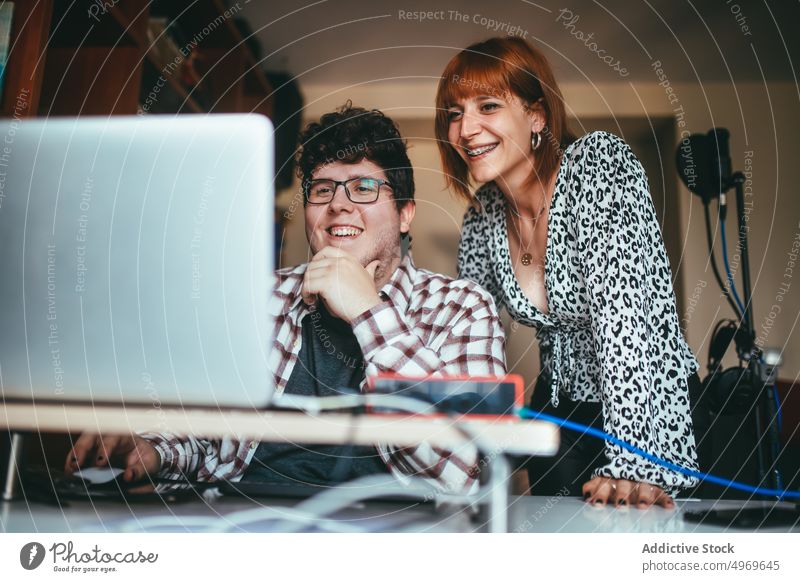 Smiling singer with producer sharing laptop at home share interact cheerful touch chin work using gadget man woman device netbook smile eyeglasses show watching