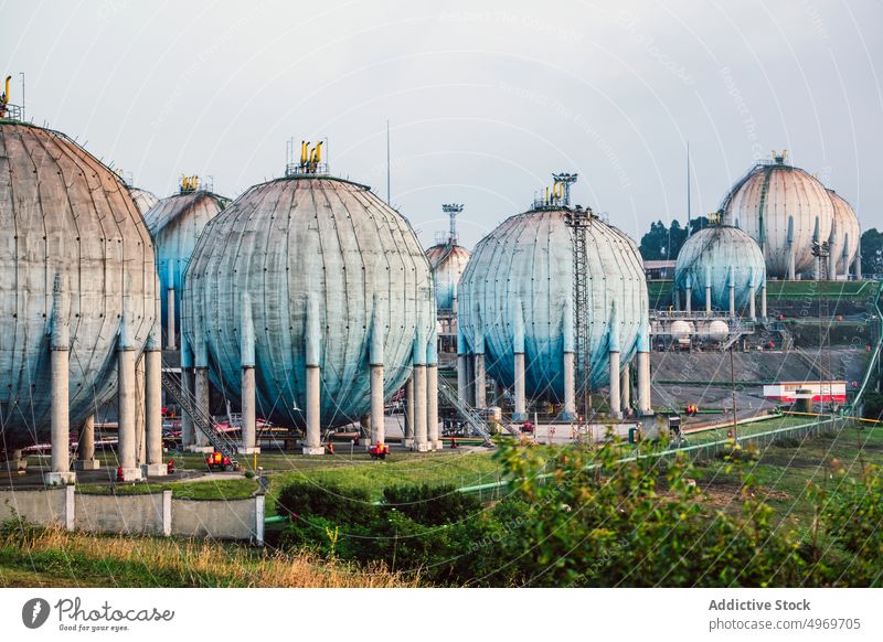 Ground environment of refinery with spherical gas tanks and trucks industrial rural construction fuel deposit container grass green meadow global warming huge