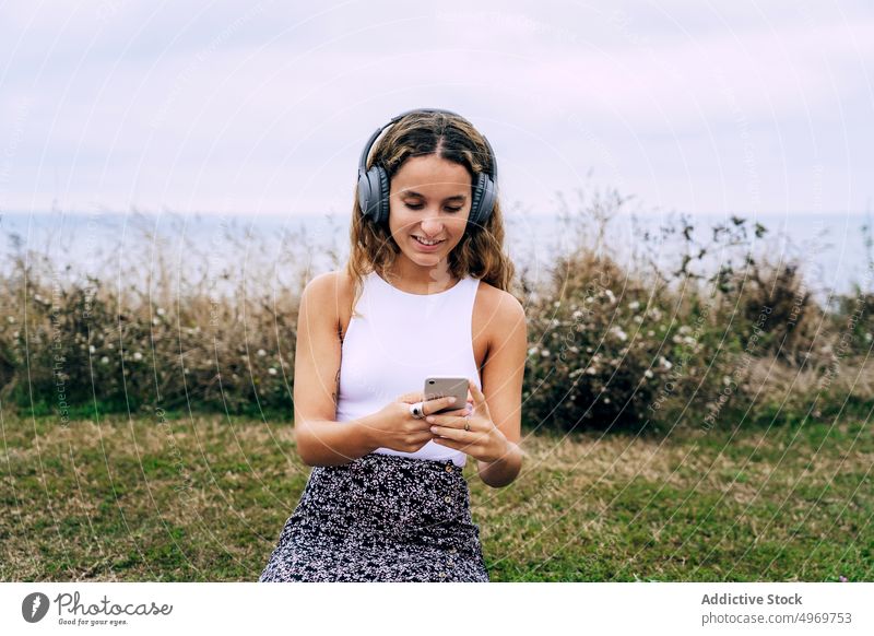Woman in headphones sitting on bricked wall with smartphone woman music using gadget device listening mobile young happy female attractive connection browsing