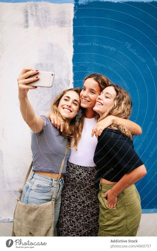 Group of pleasant women taking selfie on smartphone nearby brigh picture hugging photo camera using street meeting friendship photography walking bonding device
