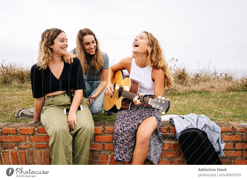Woman smiling and playing guitar to friends sitting on arched le woman ledge brick case for guitar enjoying listening young graffiti instrument design
