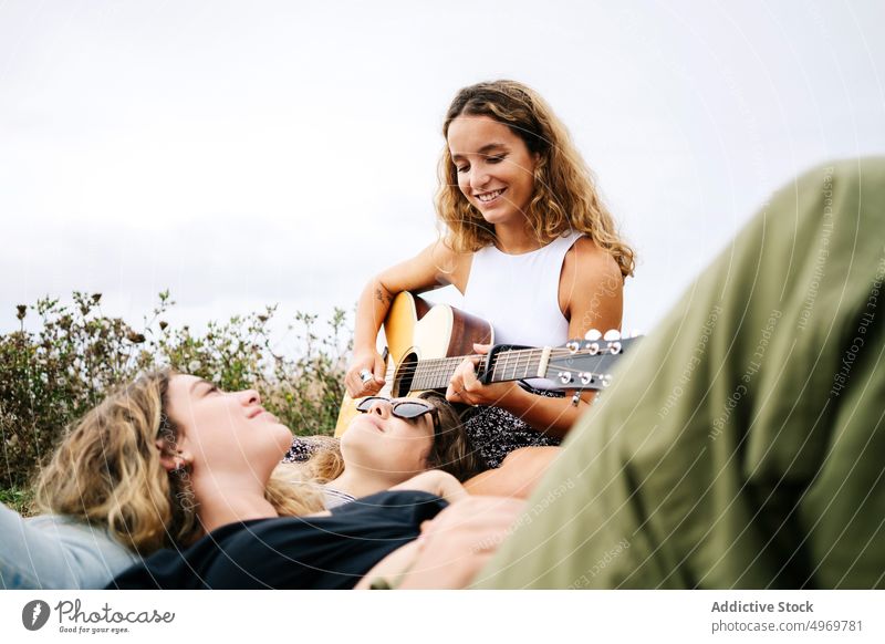 Woman smiling and playing guitar to friends in field woman enjoying listening young romantic instrument friendship cheerful female relationship together music