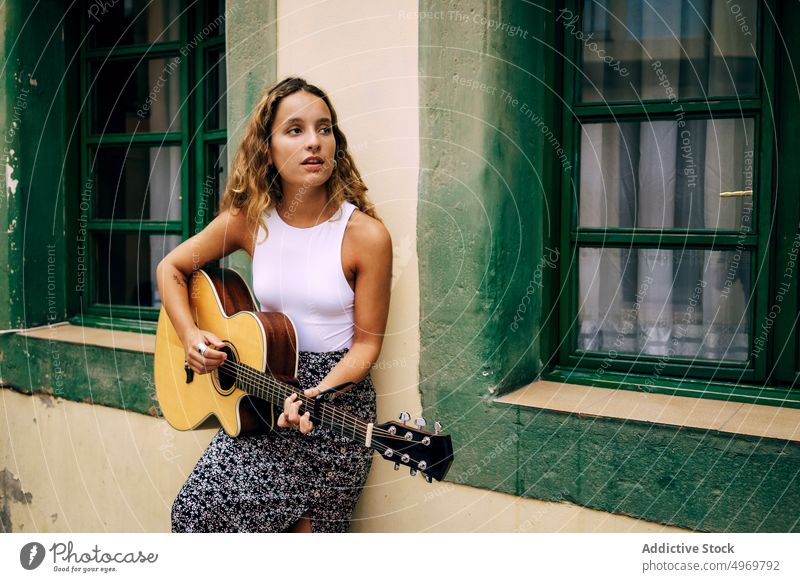 Curly woman playing guitar leaning on the wall music romantic young instrument cheerful female musical fun vacation fashion holiday casual summer creative