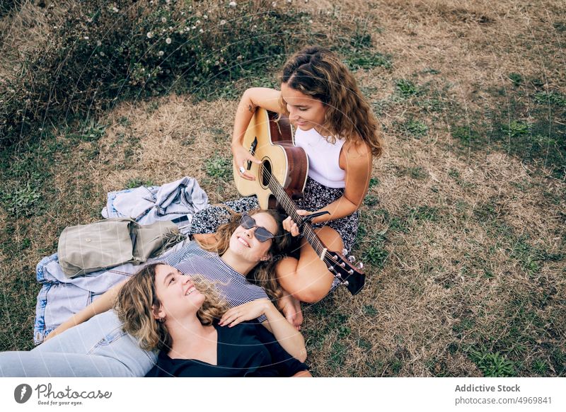 Woman smiling and playing guitar to friends in field woman enjoying listening young romantic instrument friendship cheerful female relationship together music