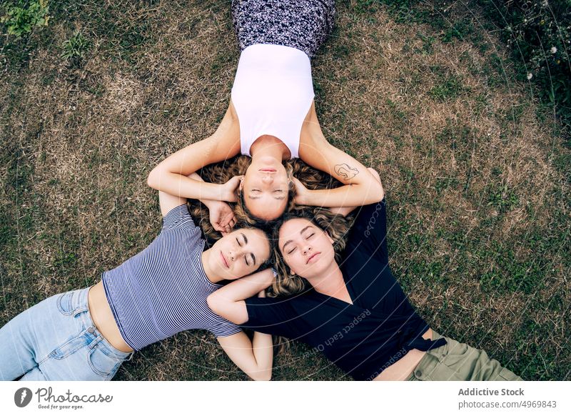 Relaxed girl friend lying in grass with heads in circle and laug women park friends lawn friendship together cheerful attractive fun group joyful adult natural