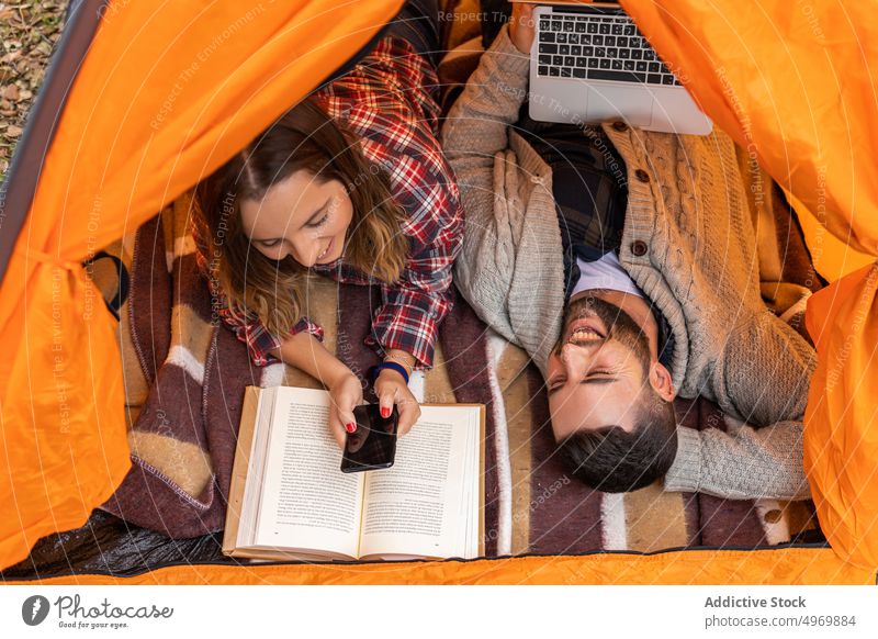 Camping couple inside tent using gadgets vacation holidays young orange laptop boyfriend active together smartphone relationship computer love browsing colorful