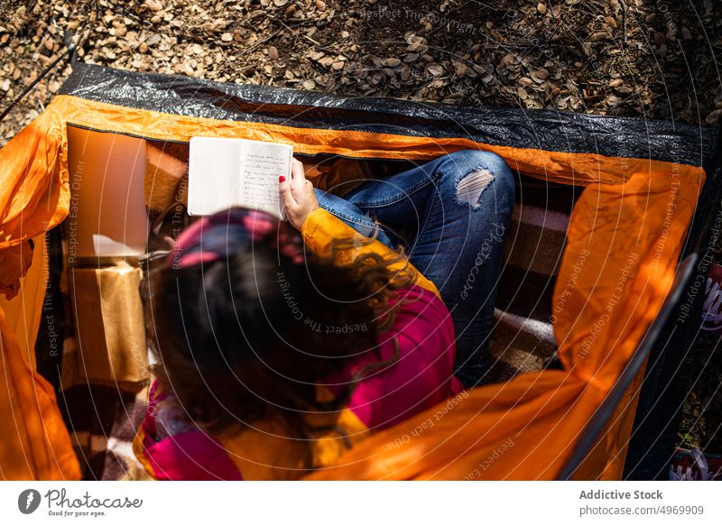 Anonymous woman sitting in tent writing notes on notebook camp enjoy grass outdoor relax forest holidays adventure field countryside vacation lifestyle tourism