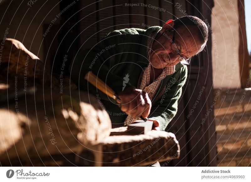 Elderly carpenter working with wood chisel hammer workshop elderly hands wrinkled equipment tool industry craft woodworker male senior mature manual job