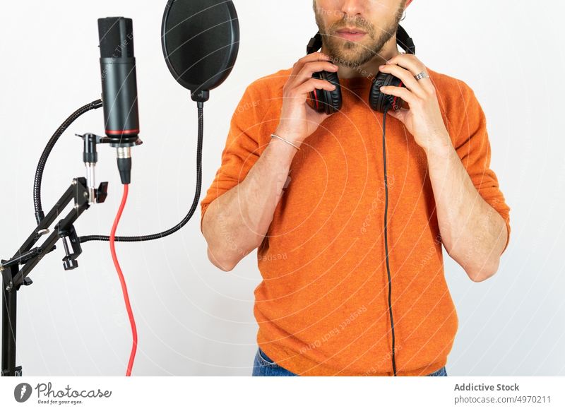 Anonymous talented man singing in studio recording song microphone industry audio music voice headphones appliance workplace male eyes closed professional job