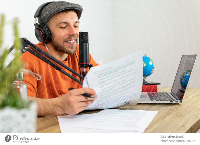 Busy man recording podcast about traveling at table with microphone radio broadcast studio audio workplace information equipment using laptop modern
