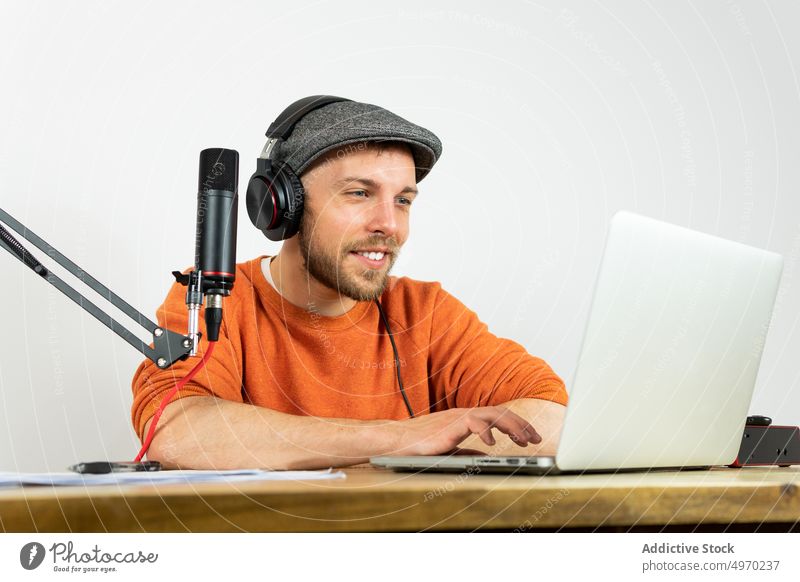 Focused man browsing on laptop and reading documents while recording studio headphones listen audio microphone workplace using paper broadcast modern radio