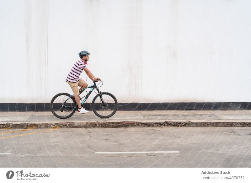 Man riding bicycle along road man ride city sidewalk street bicyclist pastime hobby male transport activity active helmet motion path walkway roadway pathway