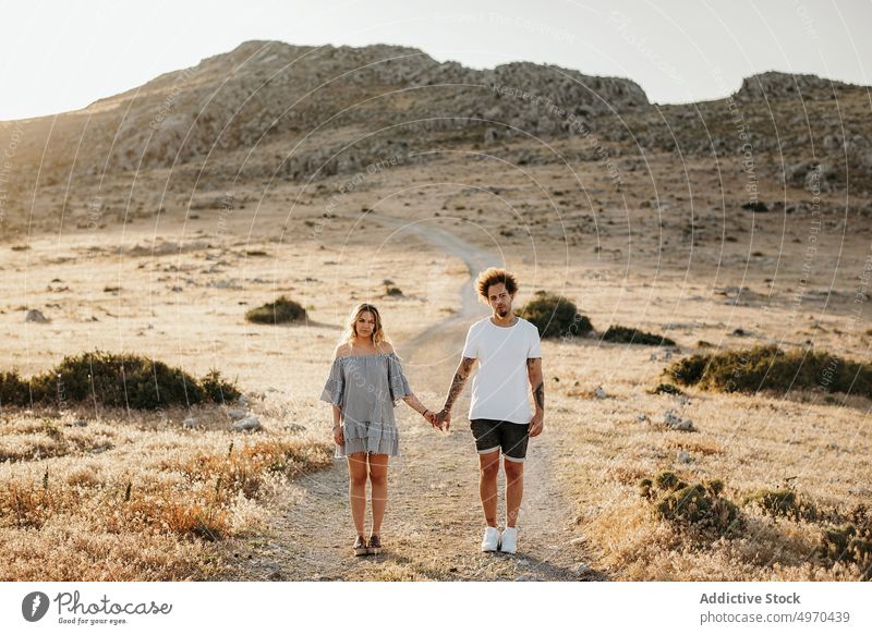 Couple holding hands while standing on footpath against rocky hill in evening couple walk romantic stroll love serious girlfriend boyfriend date weekend