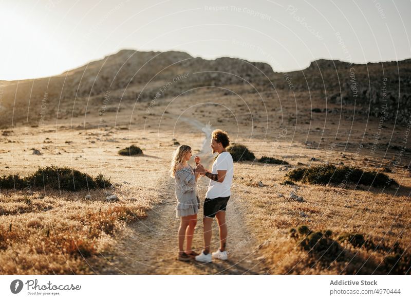 Couple holding hands while standing on footpath against rocky hill in evening couple walk romantic stroll love serious girlfriend boyfriend date weekend