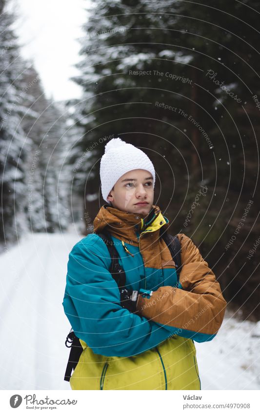 Candid portrait of a young man wearing a winter coloured jacket and a white cap during the winter season in a snowy area. Exploring new areas sport downhill