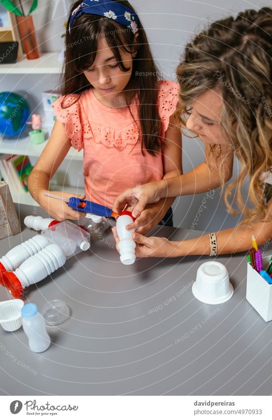 Teacher helping to girl make recycled toy robot with hot melt glue gun teacher kid children robotic reuse reduce female education school ecology copy space