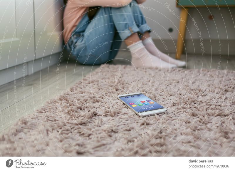 Mobile phone lying on the floor with unrecognizable sad little girl sitting behind mobile phone bedroom dangerous social media child kid harassment worried