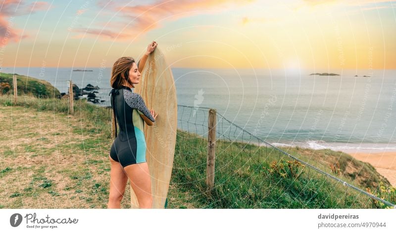 Surfer woman with wetsuit posing with surfboard looking at the beach surfer young copy space coast sunset sunlight spring suit attractive people outdoors sport