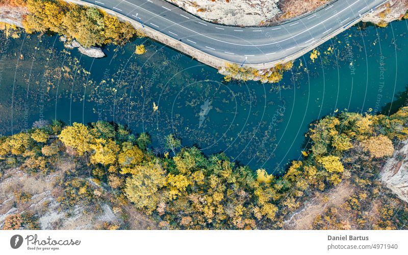 A road on a mountain slope overlooking a river with colorful vegetation and trees on the edge of the slope. Drone flight view. Background water rock sea nature