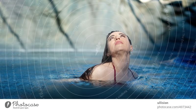 Portrait of beautiful mature woman with dark hair relaxes contend happy in holidays summer sun in the blue spa wellness whirlpool, raised eyes, looking up to the sunny sky