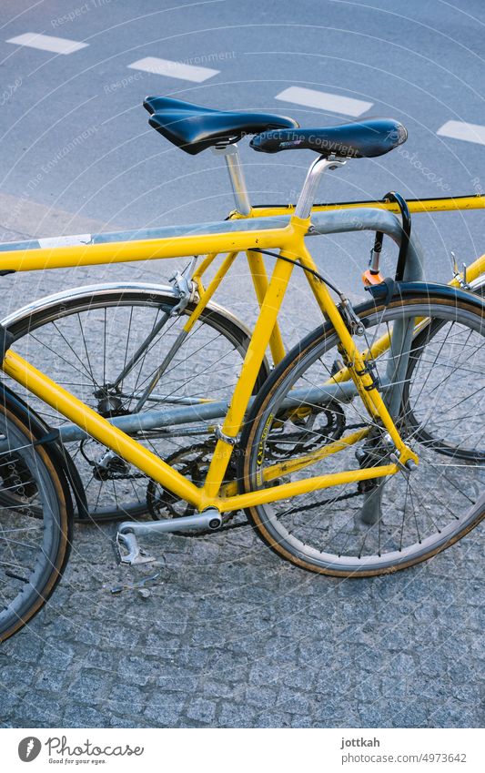 two yellow bicycles leaning against a bicycle stand Bicycle Mobility turnaround Street Yellow Colour connect Safety Transport Cycling Means of transport Town