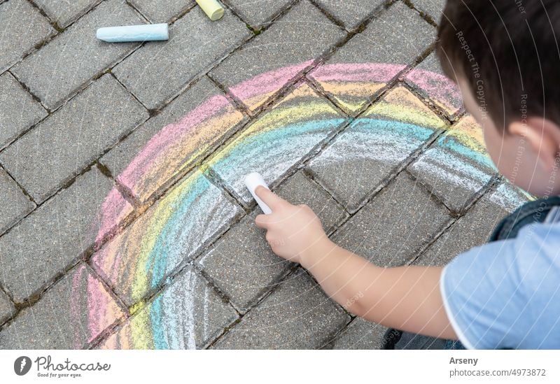 Portrait of a child drawing a rainbow on the street with colored chalk. Selective focus. Kid. A child is playing outside kid person outdoor art activity