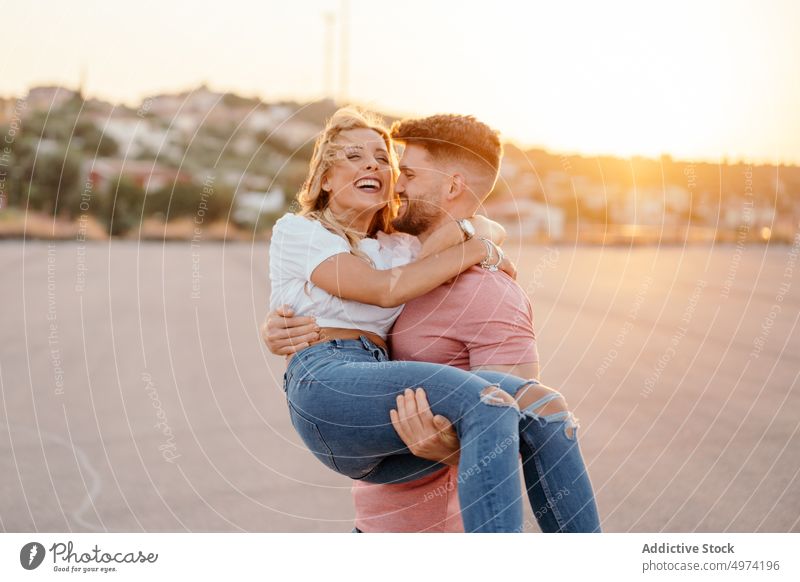 Joyful man carrying on hands girlfriend and laughing together on street at dusk couple love happy hug relationship town cheerful sunset excited tender care