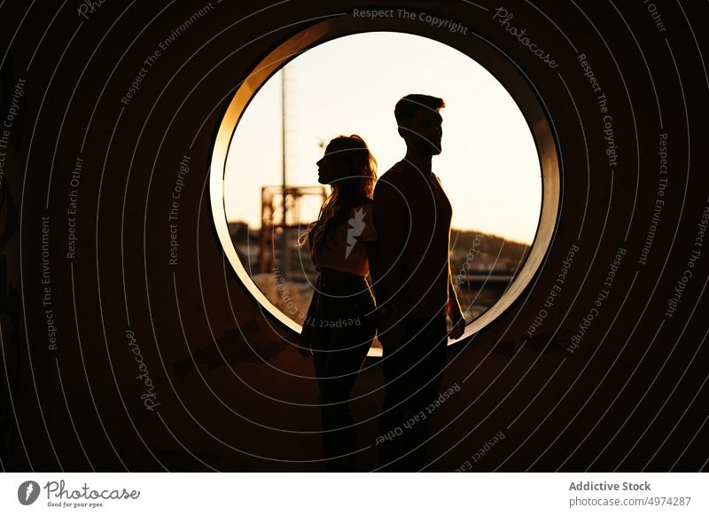 Couple standing back to back against window during sunset couple relationship joy architecture fondness hole round boyfriend girlfriend bonding date relax