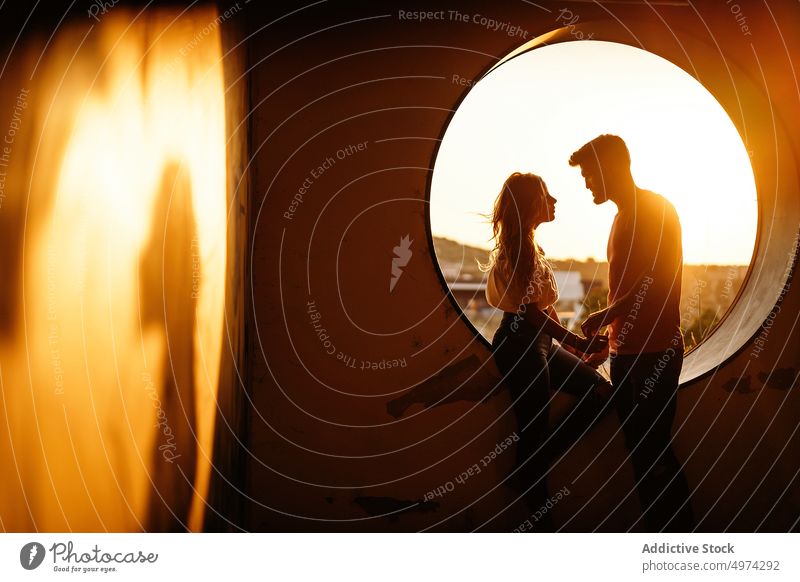 Joyful adult couple holding hands and smiling each other against window during sunset laugh relationship joy cheerful architecture fondness hole round boyfriend