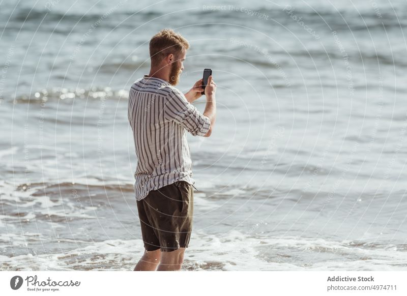 Bearded man taking photos with his mobile on the beach phone person nature travel picture ocean technology landscape sea summer cell boy camera beard sun blue