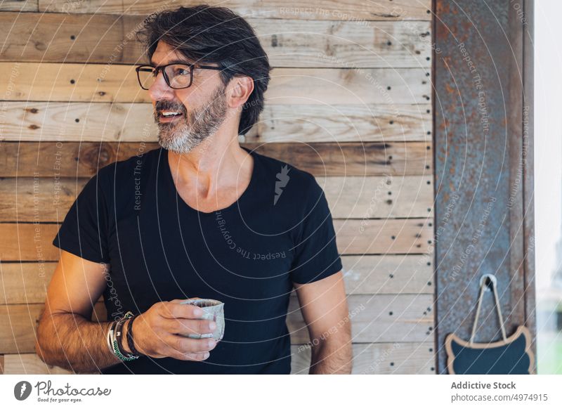 Smiling senior man drinking morning coffee content smile peace contemplate cheerful calm cup cozy style casual glasses aged enjoy happy stand wooden wall