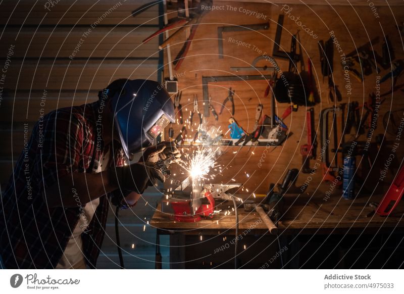 Male cutting piece of metal in modern workshop man helmet angle grinder spark worker equipment using workplace instrument mechanic craftsman process industry
