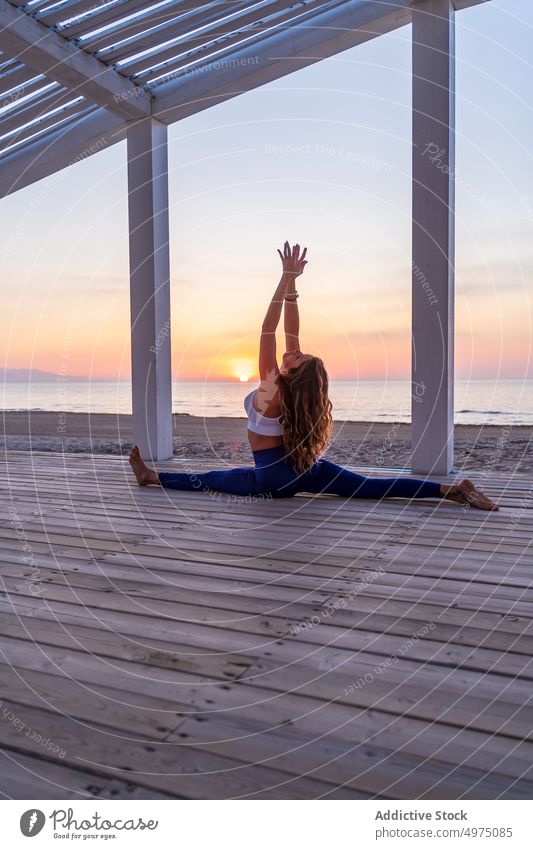Flexible woman doing yoga at seaside during sunrise pose crescent lunge terrace tranquil sportswear practice wooden anjaneyasana serene healthy harmony calm