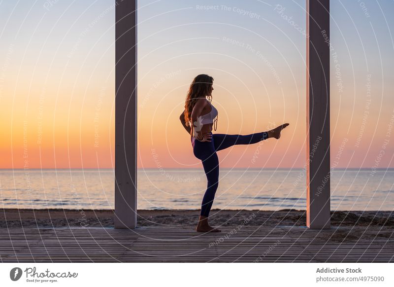 Flexible woman doing yoga at seaside during sunrise pose terrace tranquil sportswear practice wooden anjaneyasana serene healthy harmony calm dawn peaceful