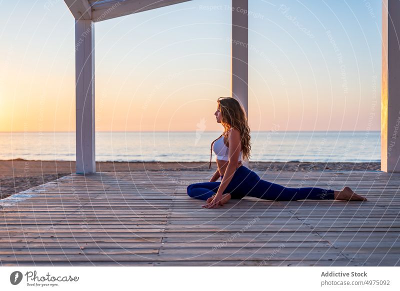 Woman practicing yoga in Pigeon pose on seashore pigeon pose woman meditate practice sunrise namaste tranquil gesture wooden promenade seaside asana