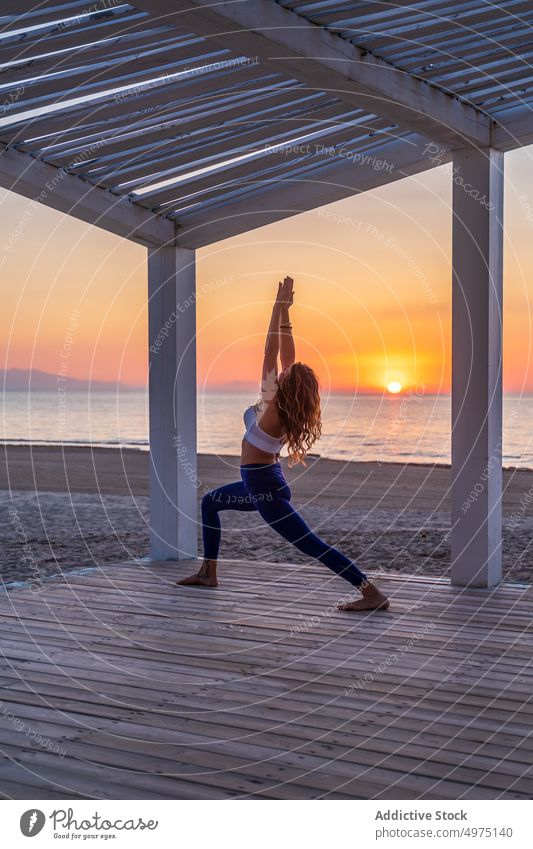 Flexible woman doing yoga at seaside during sunrise pose crescent lunge terrace tranquil sportswear practice wooden anjaneyasana serene healthy harmony calm