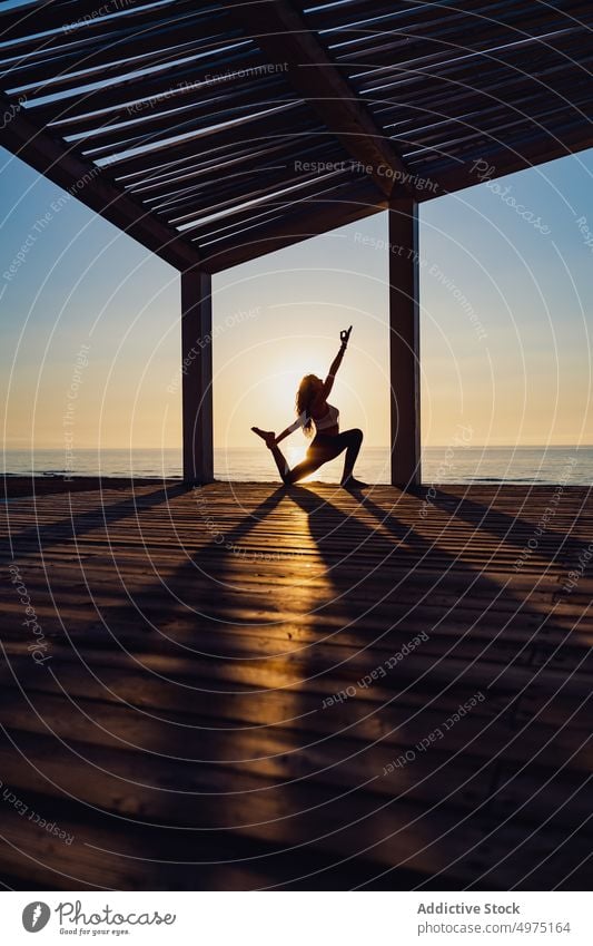 Tranquil woman doing yoga in Warrior pose during sunrise warrior seaside practice tranquil silhouette dawn wooden terrace healthy harmony relax asana