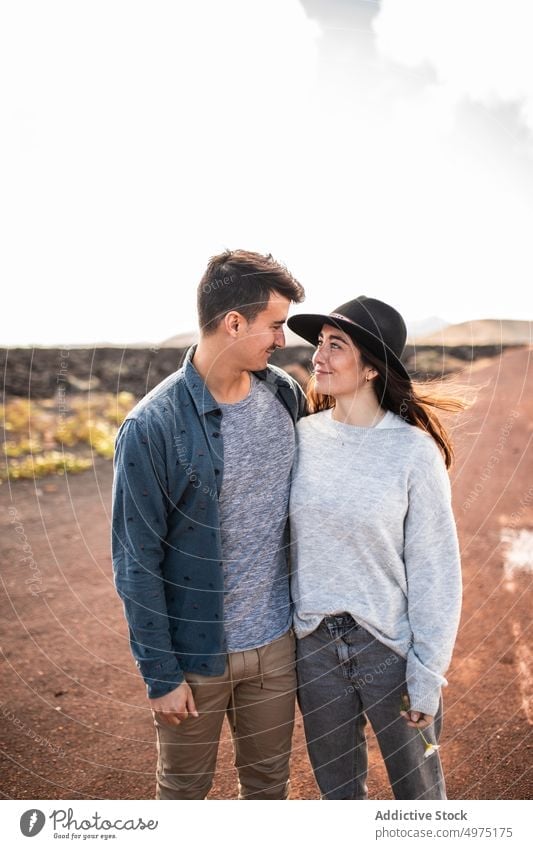 Smiling young ethnic couple hugging on rural road on sunny day cuddle smile trip romantic together love affection fondness style volcanic terrain boyfriend