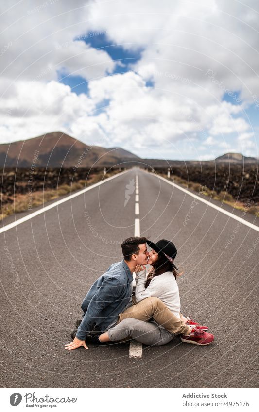 Beloved young ethnic couple sitting on road and kissing during holidays in Lanzarote romantic traveler road trip mountain affection nature journey relationship