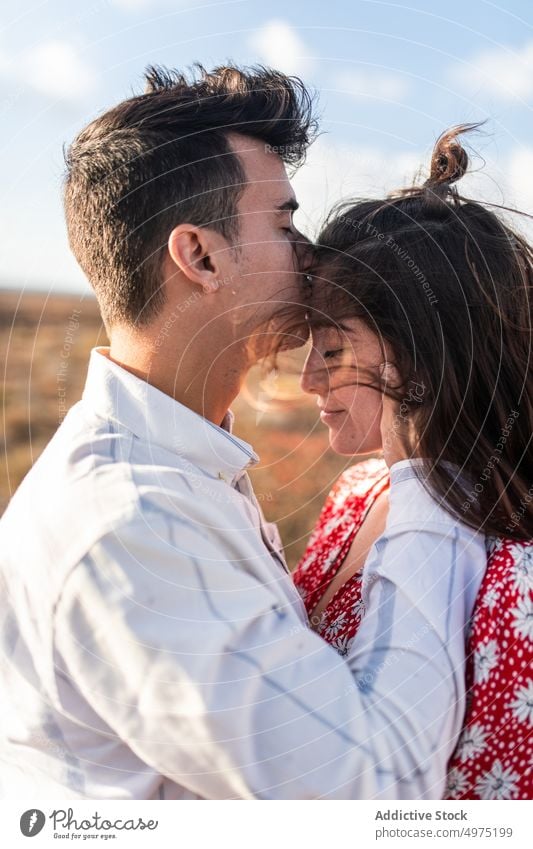 Young man kissing forehead of girlfriend with closed eyes in nature couple touch face romantic eyes closed love field together affection date calm fondness