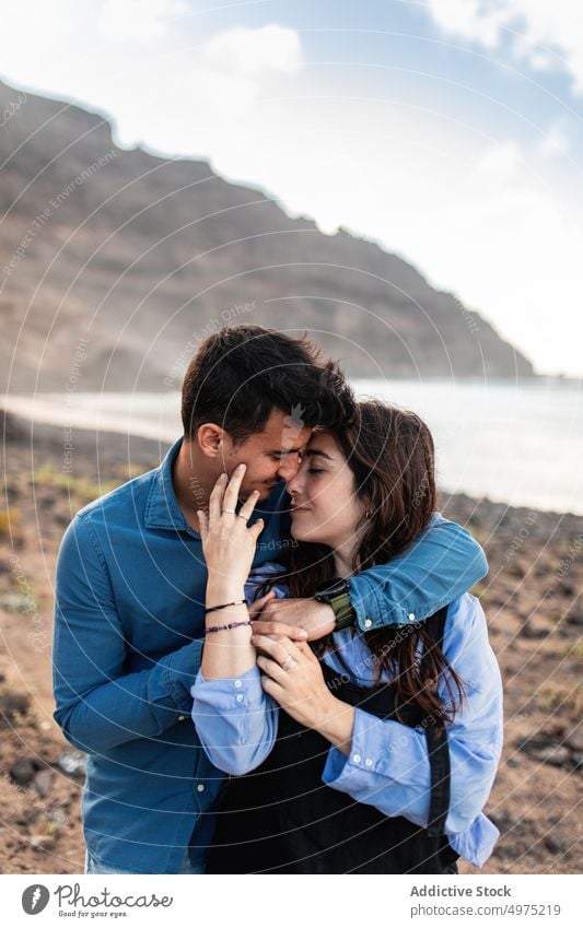 Dreamy young ethnic couple cuddling on sandy terrain in mountainous valley at sunset embrace nature love relax beach together relationship affection spend time