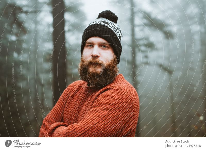 Bearded guy in sweater and hat near fir trees man forest rain coat cold weather water drop rainy bearded thoughtful wood thinking young countryside walking park