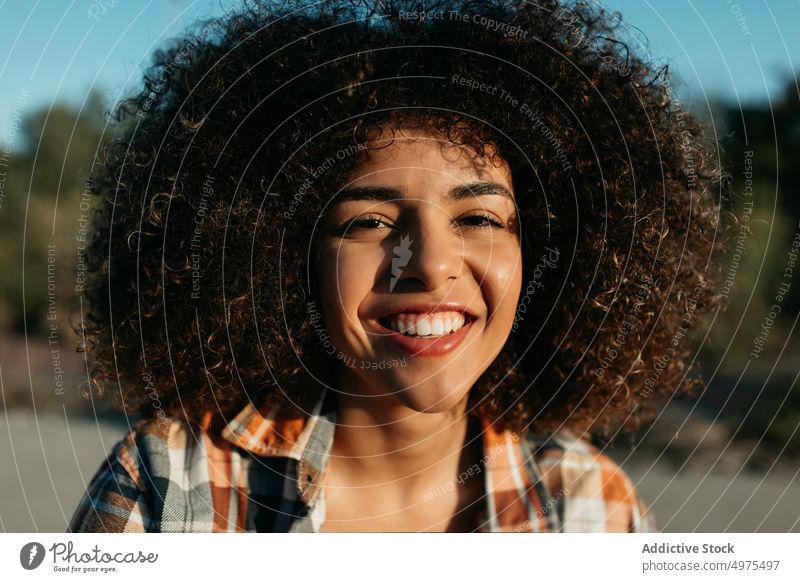 Charming black woman with curly hair smiling on street hipster sunset afro hairstyle content charming smile checkered shirt female ethnic african american enjoy
