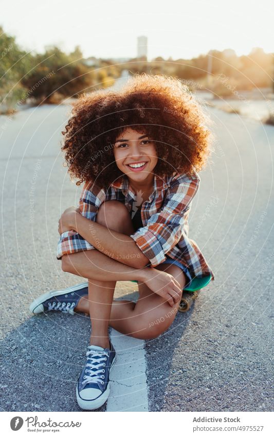 Delight African American woman sitting on penny board on the asphalt road summer skater street cool millennial afro trendy tranquil hipster sunny female ethnic