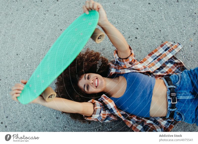 African American woman lying down with penny board on the asphalt road summer skater street millennial afro trendy tranquil hipster sunny female ethnic