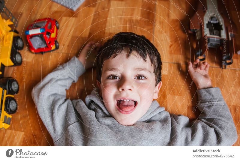 Happy boy playing with toy cars kid vehicle happy cheerful portrait floor game little lying child male childhood playful entertain home smile laugh excited joy