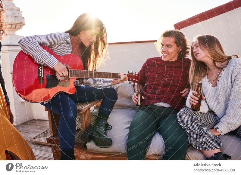 Cheerful diverse friends gathering on terrace and playing guitar party content beer music sing cheerful rooftop together guitarist friendship smile delight