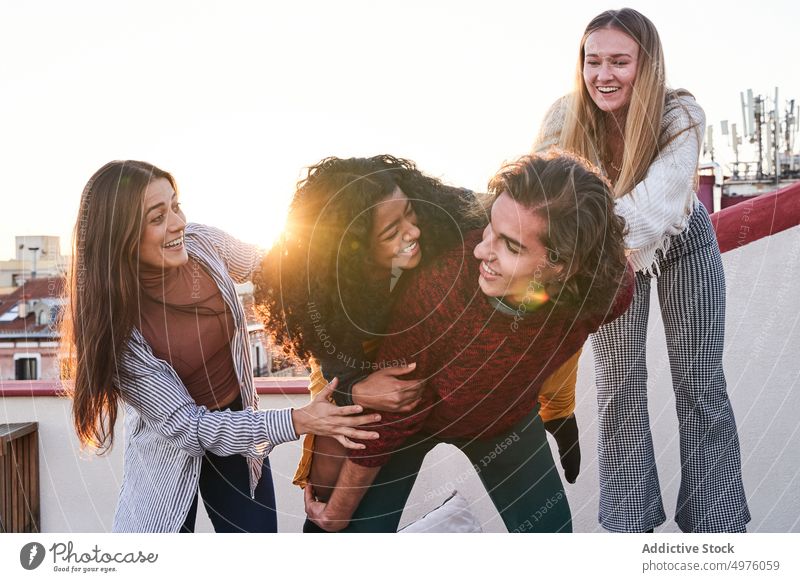 Cheerful man piggybacking ethnic female friend during party on terrace having fun rooftop toothy smile gather excited group carefree laugh cheerful together