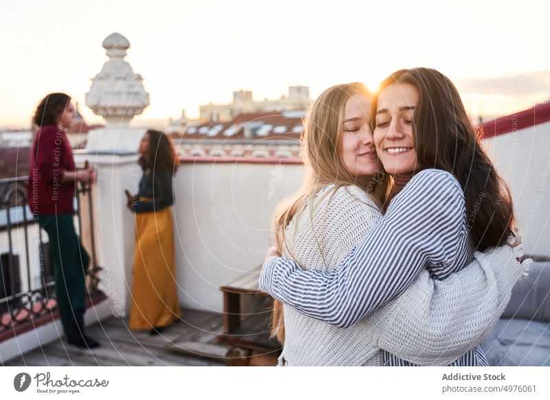 Cheerful women hugging on terrace during party friend toothy smile joyful rooftop embrace cheerful hangout together friendship twilight evening relationship