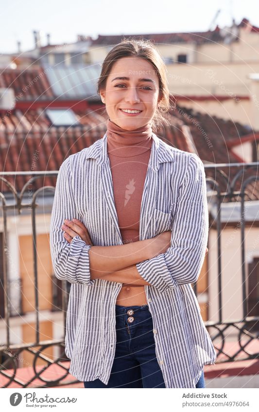 Smiling woman standing with arms folded on building rooftop cheerful toothy smile terrace content town posture happy casual young optimist city female summer